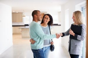 Female Realtor Shaking Hands With Couple Interested In Buying House